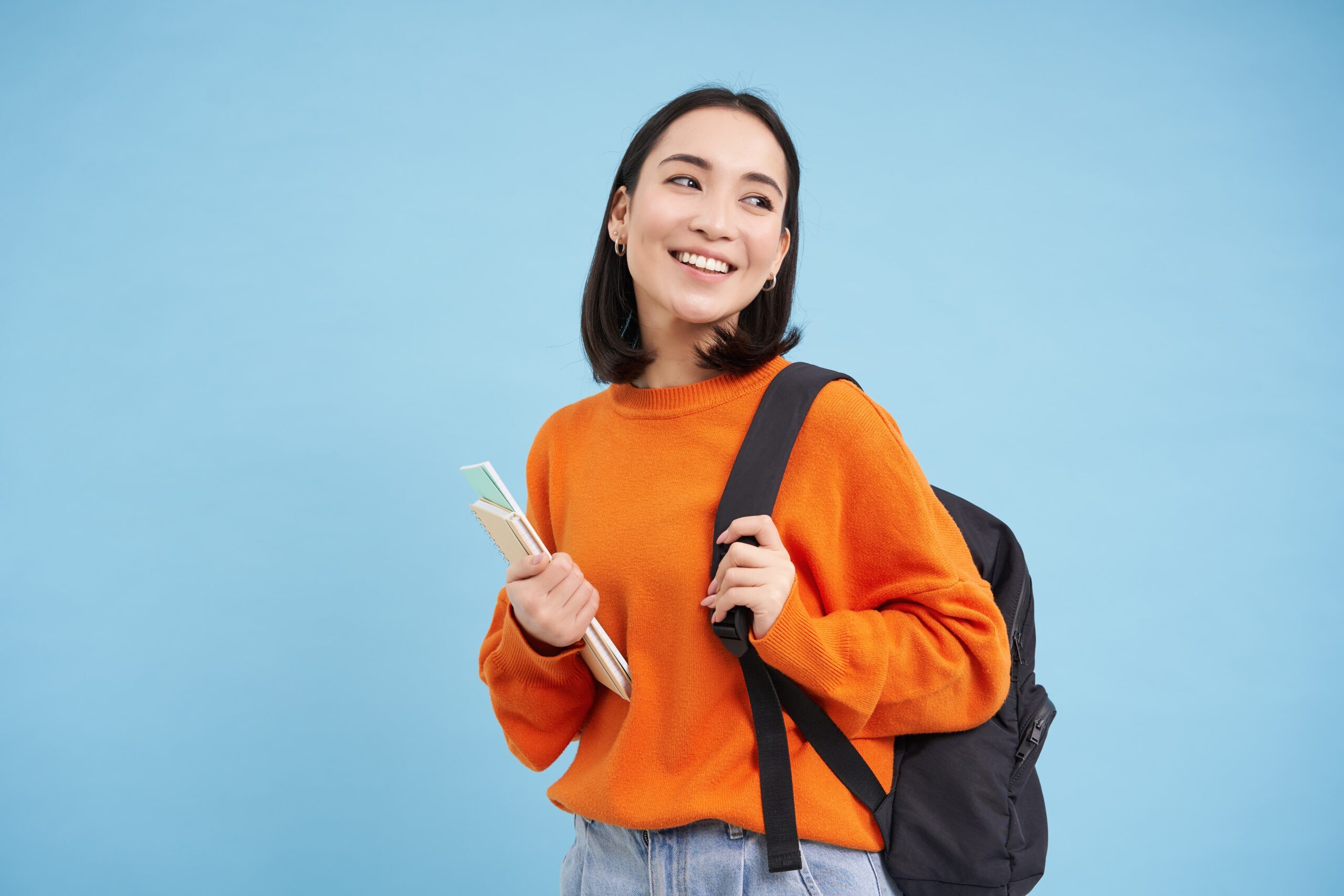 education-students-smiling-young-asian-woman-with-backpack-notebooks-posing-against-blue-bac-min