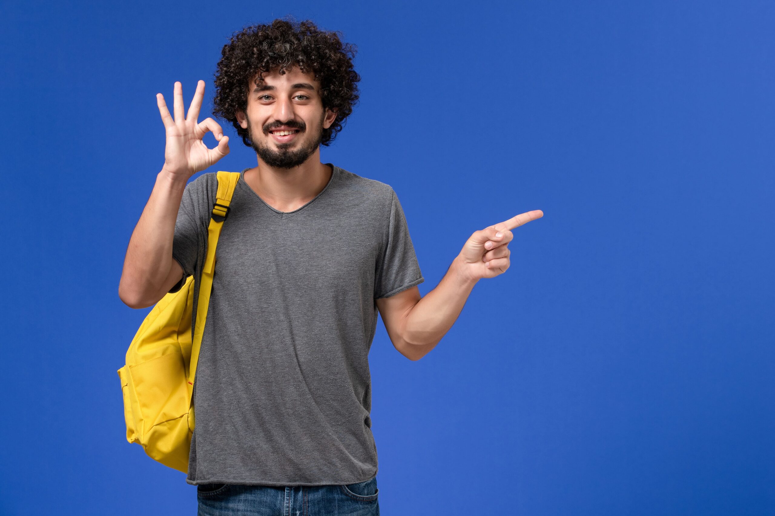 front-view-young-male-grey-t-shirt-wearing-yellow-backpack-smiling-blue-wall (1)